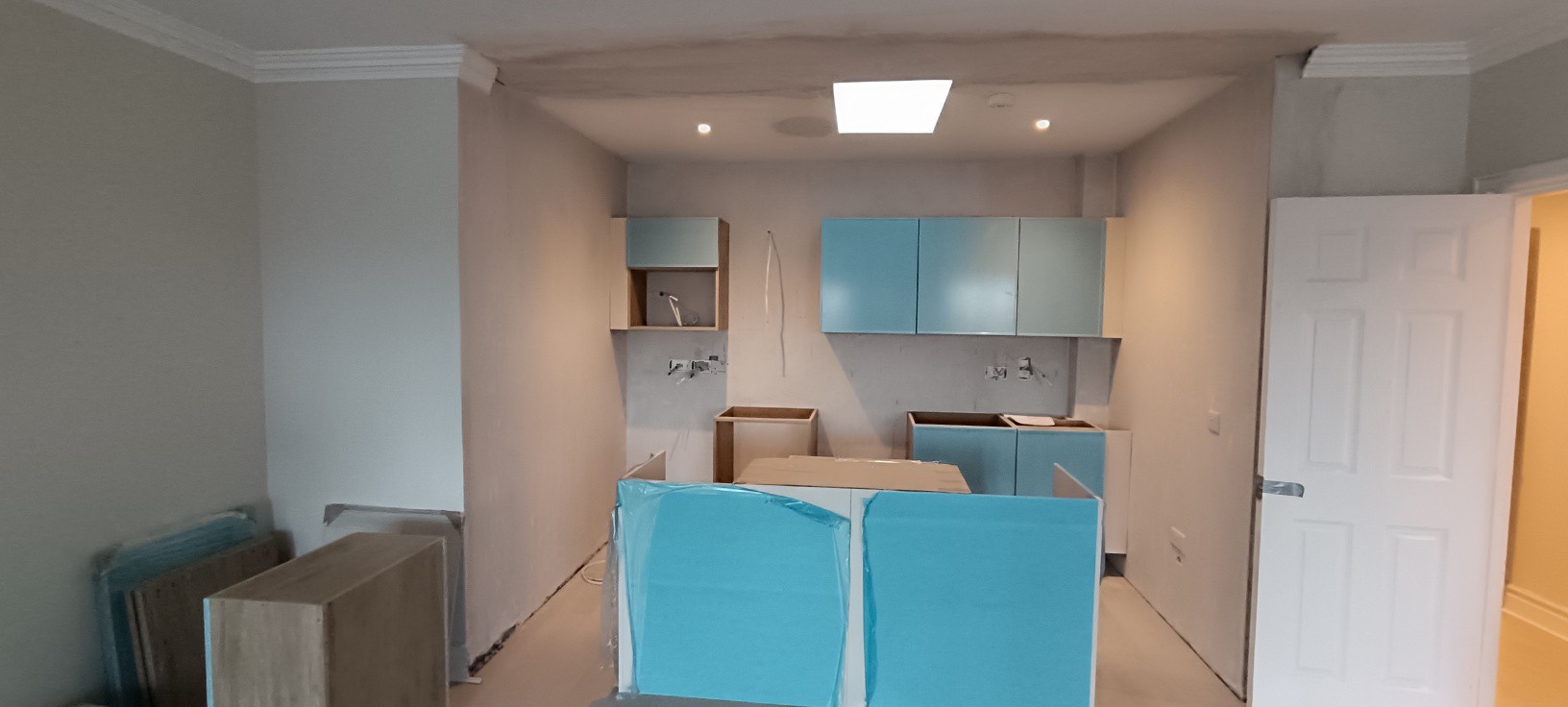 Teal kitchen units mid-installation in open plan room